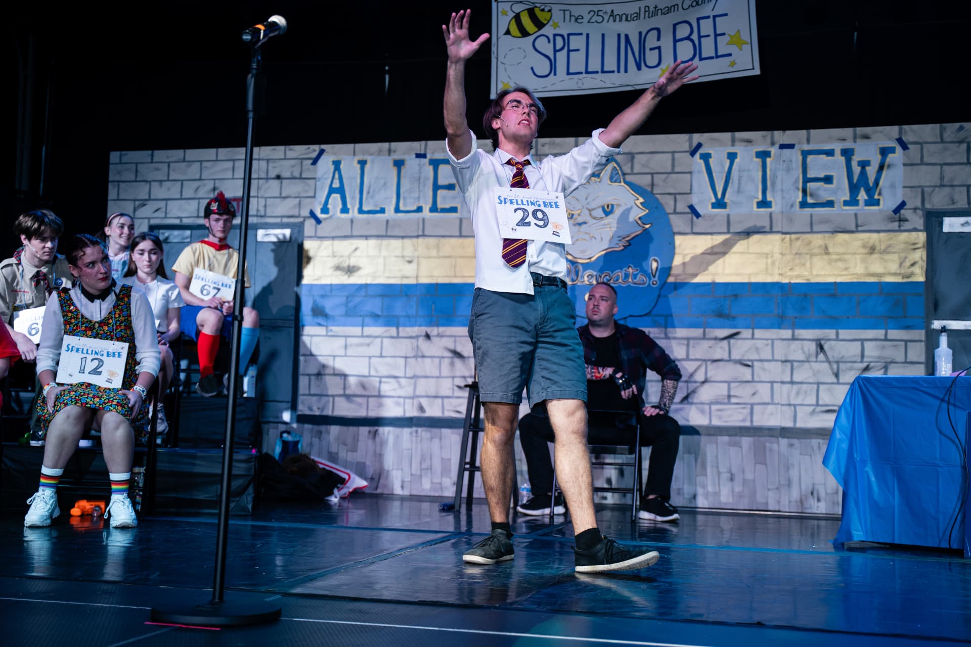 Richard Jordan with both arms raised before the judges and seated spellers during Putnam County Spelling Bee