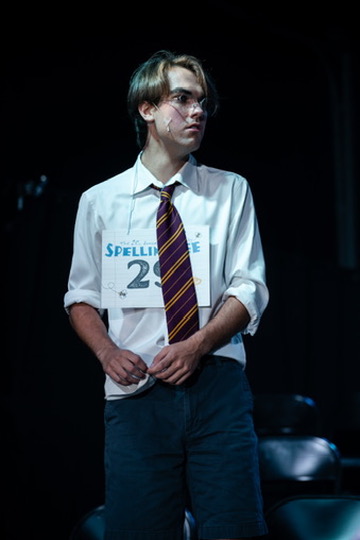 Richard Jordan standing with his number 29 card in a quiet spotlight moment during Putnam County Spelling Bee