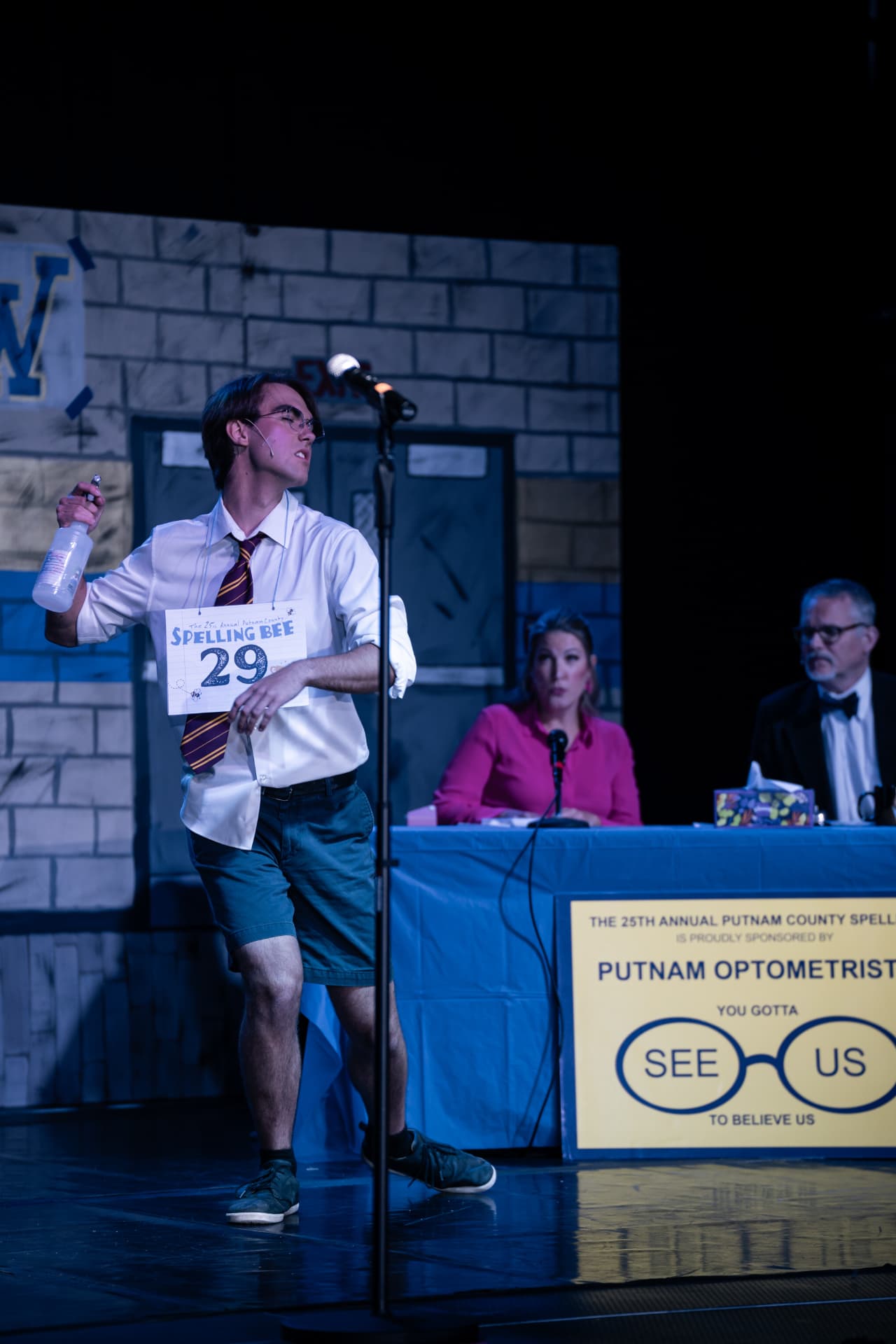 Richard Jordan performing on the gymnasium set of Putnam County Spelling Bee with the judges at the table