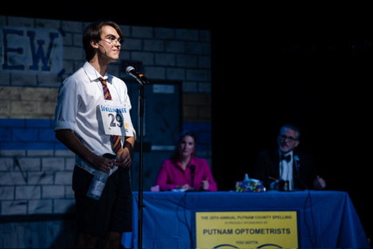 Richard Jordan spelling at the microphone with the judges' table behind him