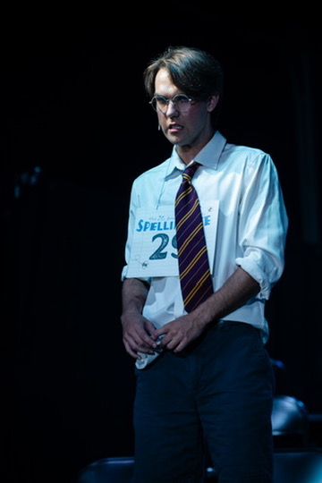 Richard Jordan adjusting his cuffs in a moody spotlight during Putnam County Spelling Bee