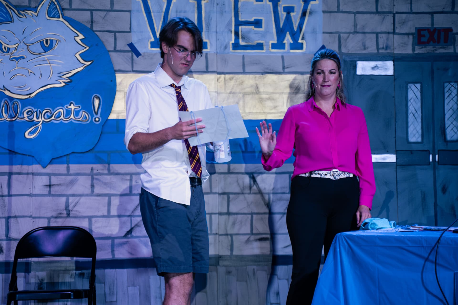 Richard Jordan reading a note from the judge beside the judges' table in Putnam County Spelling Bee