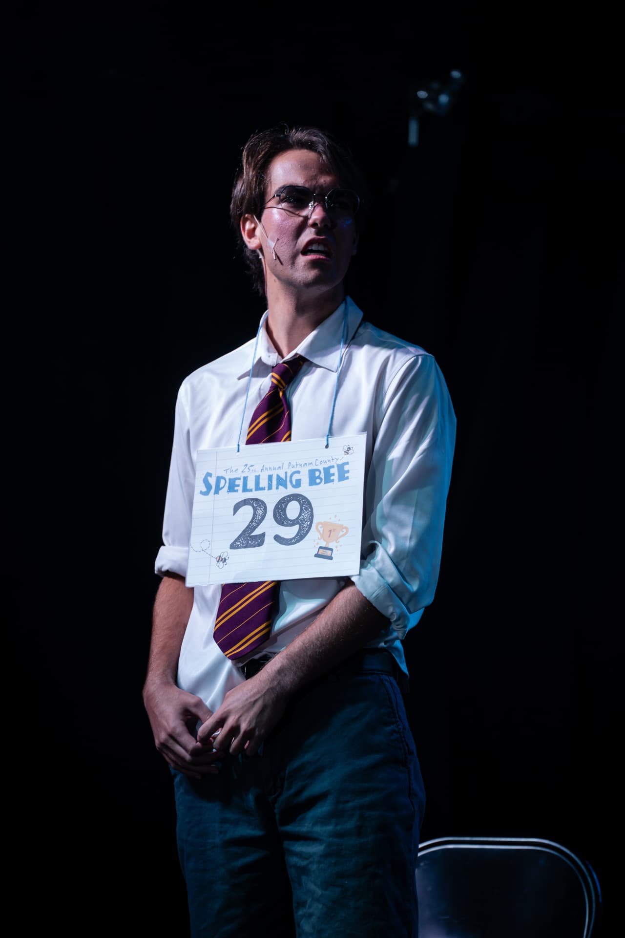 Richard Jordan as William Barfée in the spotlight wearing his Spelling Bee number 29 card